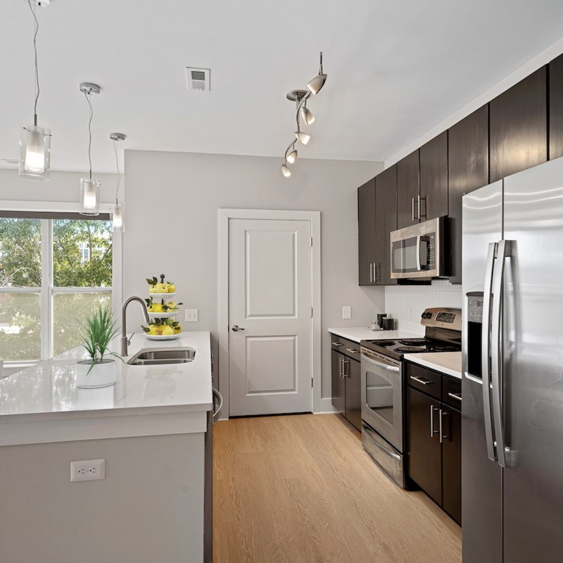 Modern kitchen interior at Hawthorne 808 featuring stainless steel appliances, dark wood cabinetry, and a central island with bar stools under stylish pendant lighting.